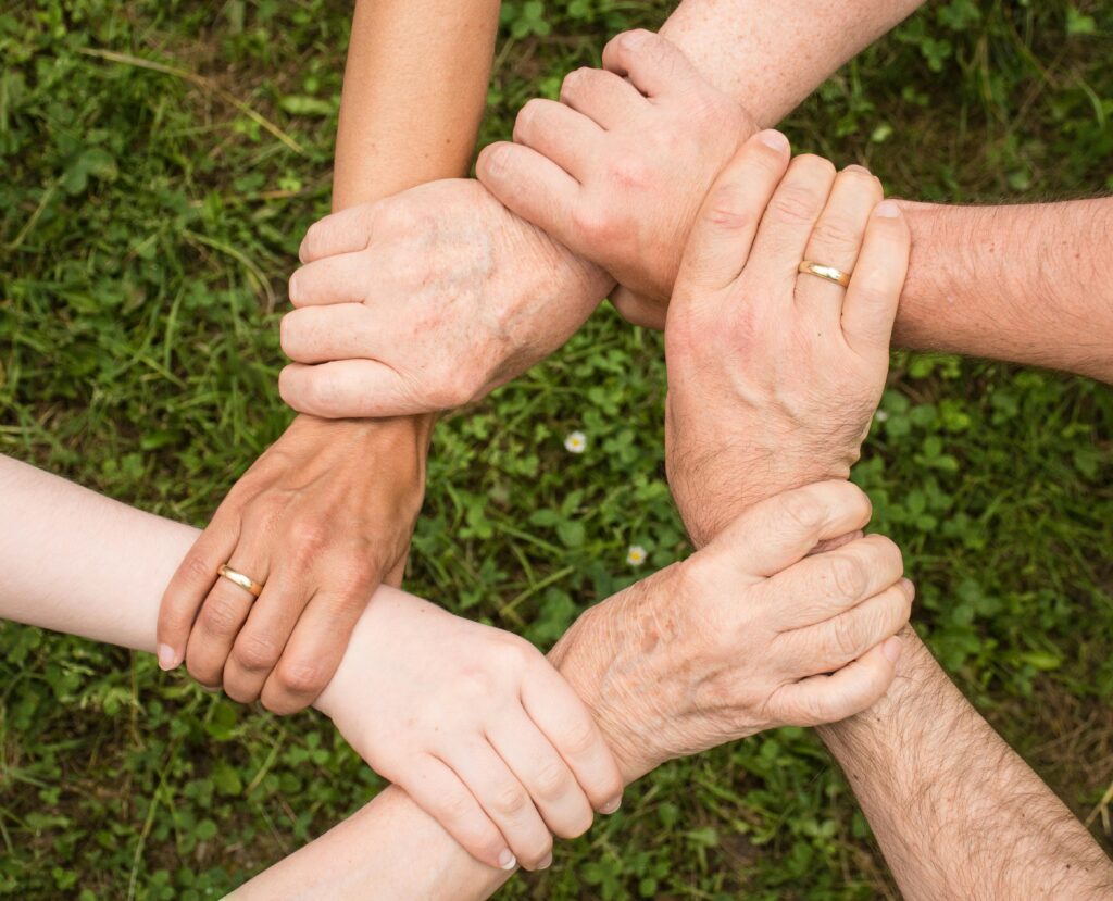 Close-up of diverse hands forming a connection, symbolizing teamwork and unity outdoors.